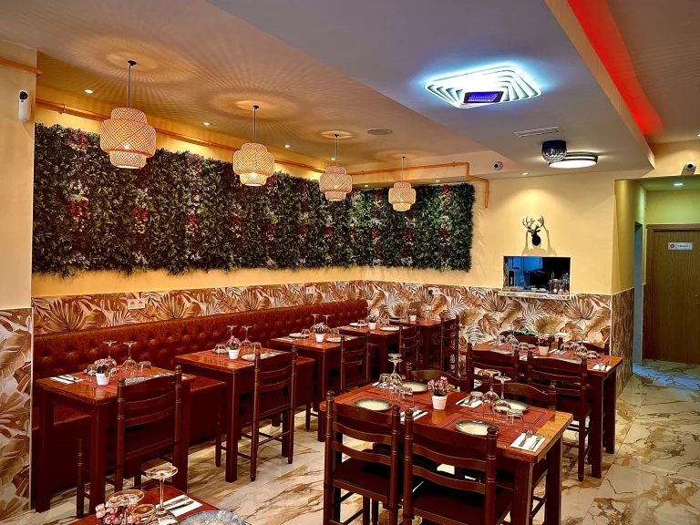 Comedor de Tastari Mediterrani con banco corrido rojo, mesas preparadas y una pared vegetal