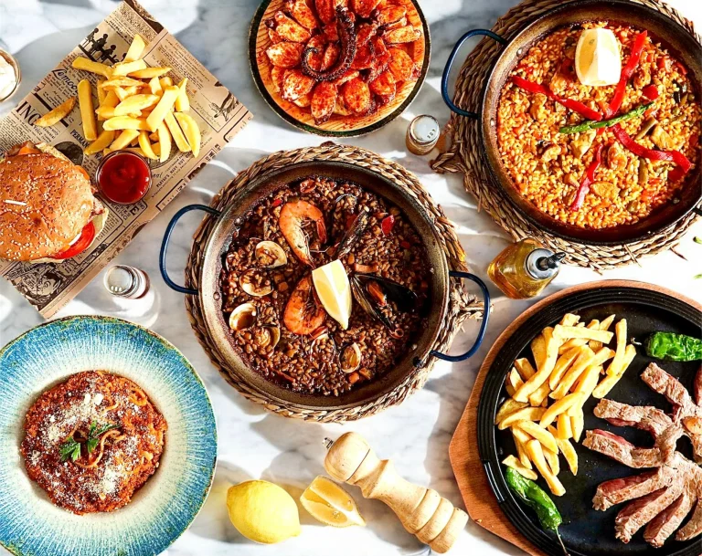 Mesa vista desde arriba con paella de verduras, arroz negro, pulpo, carne a la parrilla y patatas fritas